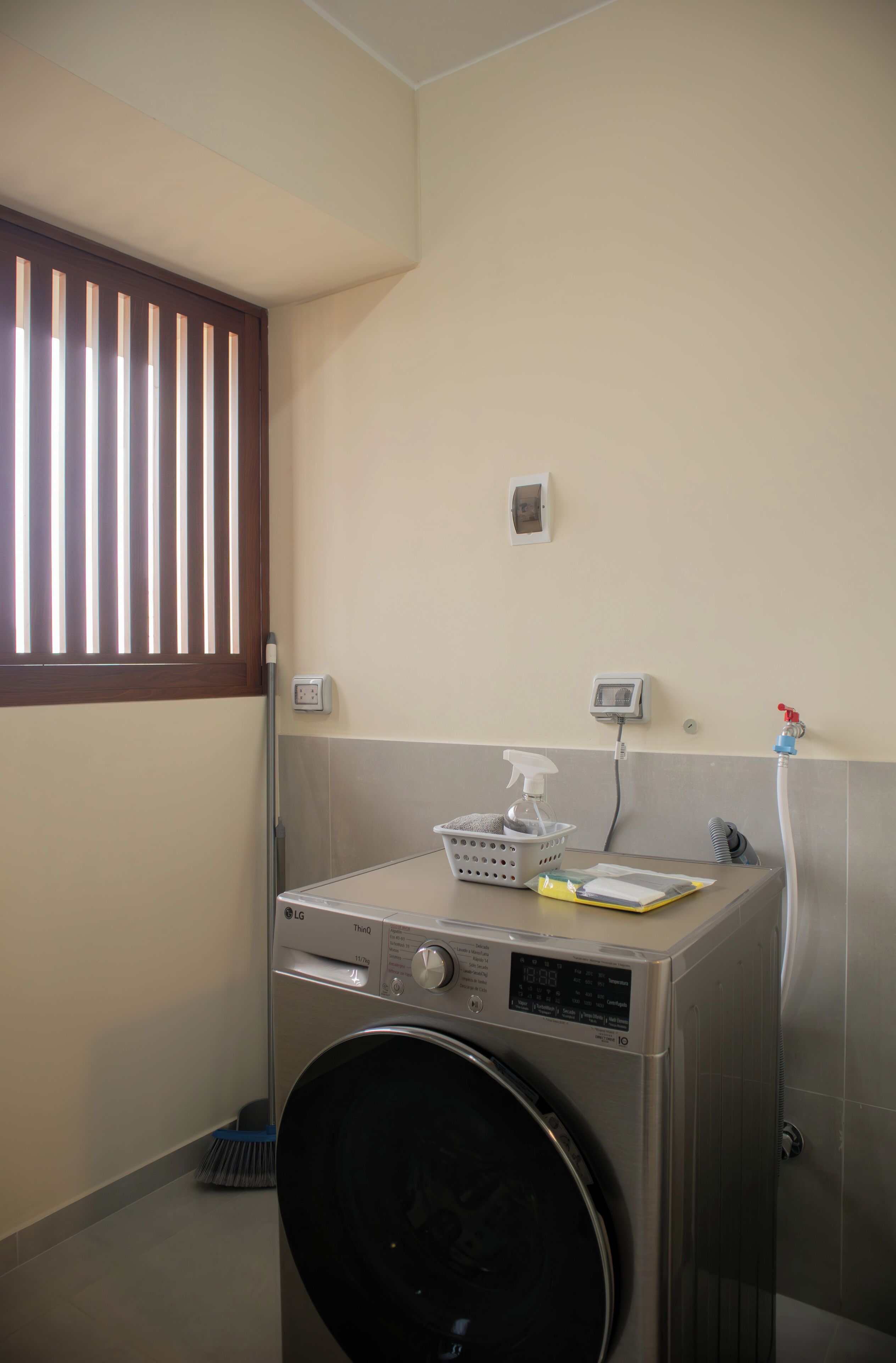 A compact laundry area with a front-loading washing machine, a drying rack, and a wall-mounted control panel.