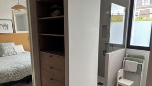 Une chambre à coucher comprenant un lit, une armoire et une salle de bain avec une douche, un porte-serviettes et une chaise.