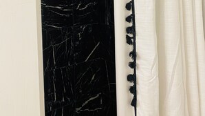 Un área de ducha con cortina blanca y pared de mármol negro.