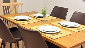 Une table à manger dressée avec des assiettes, des couverts et un petit vase contenant des plantes vertes.