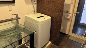 Une petite salle de bain avec un lavabo en verre, un lave-linge blanc, un porte-serviettes et des toilettes.