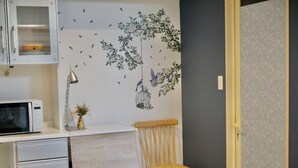 Une cuisine équipée d’un four à micro-ondes, de placards, d’une chaise en bois et d’un mur décoré d’un motif sur le thème de la nature.