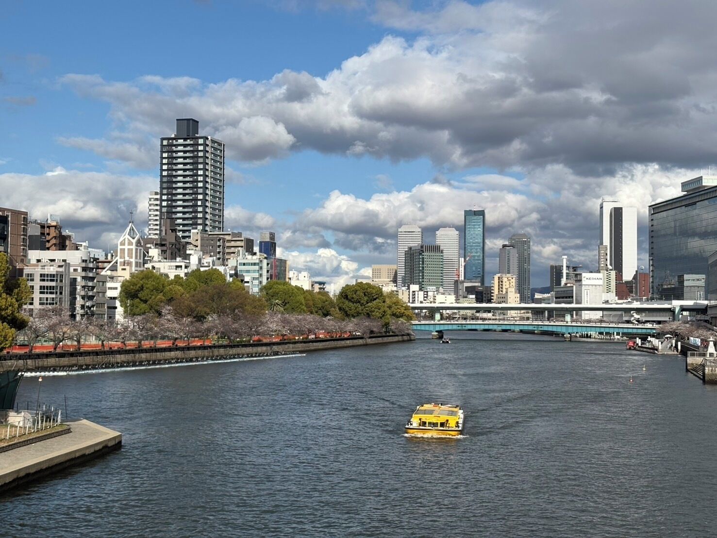 A cityscape with a river, a yellow boat, and modern buildings.