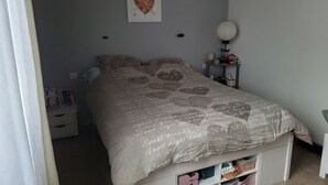 Un dormitorio con cama, mesita de noche, lámpara de pared y estante con cajas de almacenamiento.