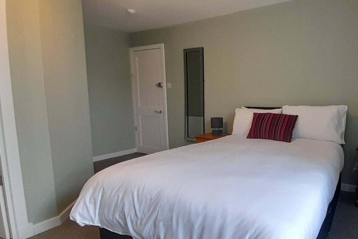 Une chambre à coucher avec un lit, des tables de chevet, un miroir et une porte.