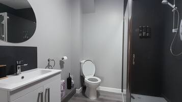 Un baño moderno con lavamanos, espejo, inodoro y ducha blancos.