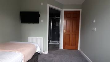 Un dormitorio con una cama, un televisor instalado en la pared y una puerta que da a un pasillo.