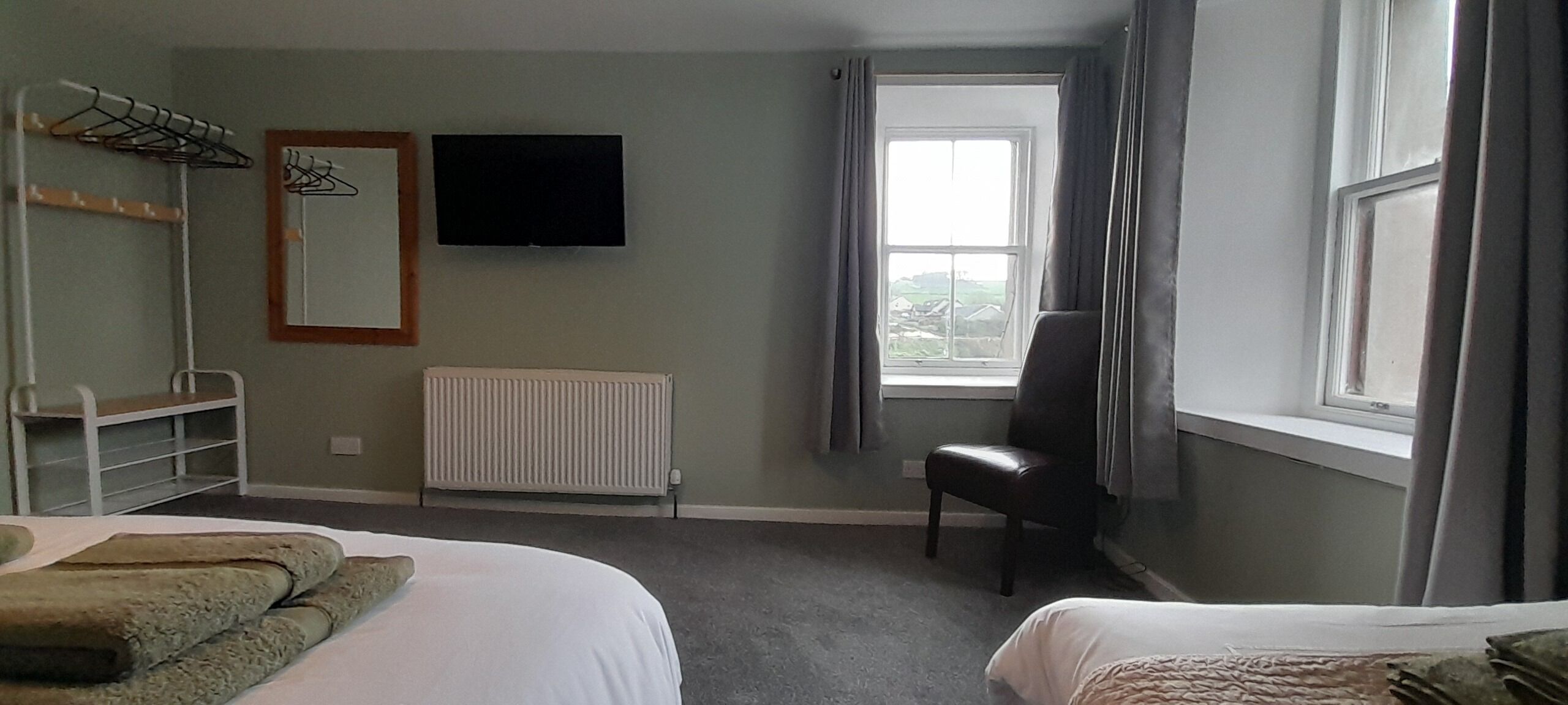 A hotel room with two beds, a radiator, a TV, a chair, and a window with curtains.