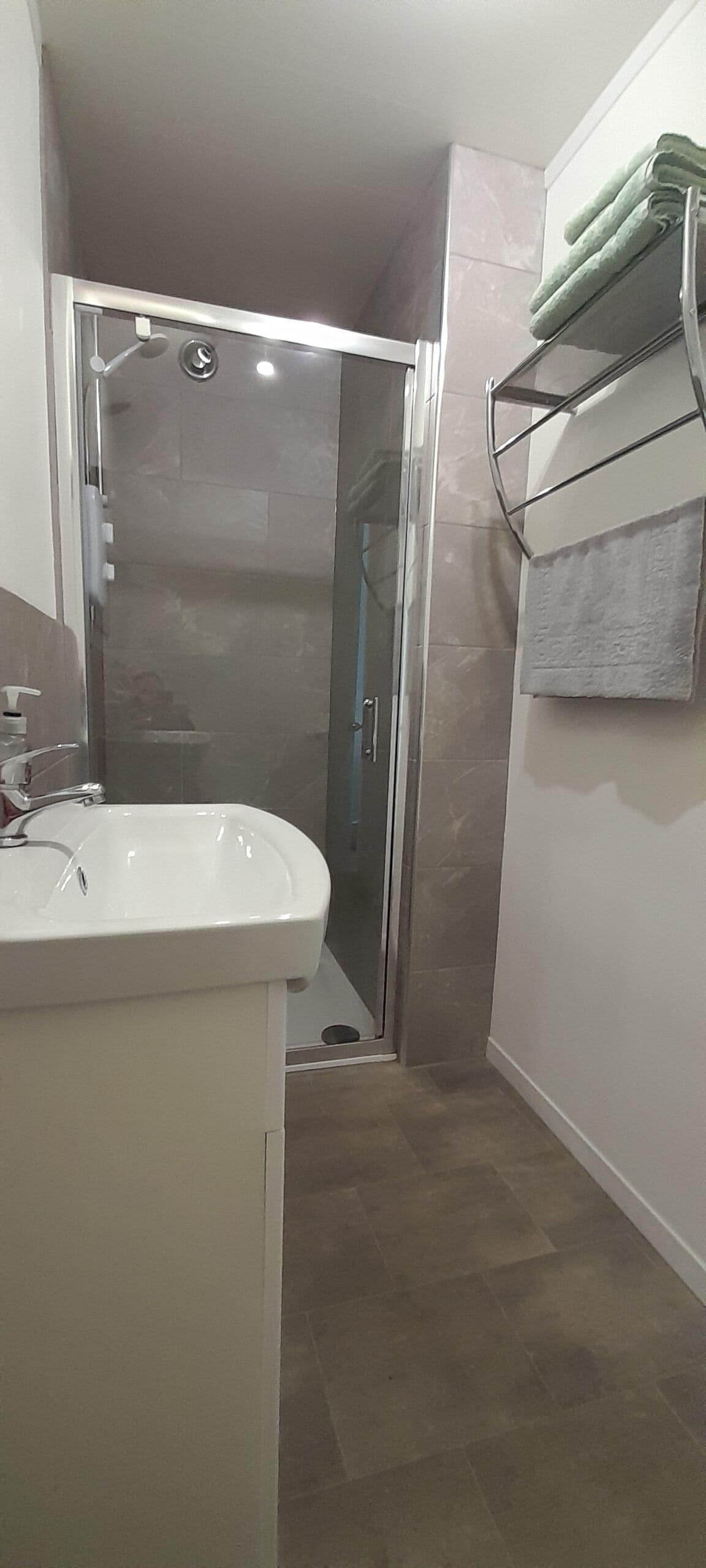 Ein Badezimmer mit einer Duschkabine, einem weißen Waschbecken und einem Handtuchhalter mit zwei Handtüchern.