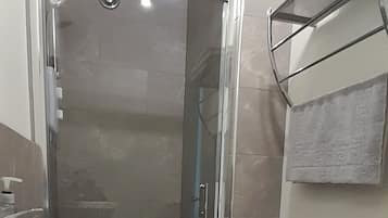 Ein Badezimmer mit einer Duschkabine, einem weißen Waschbecken und einem Handtuchhalter mit zwei Handtüchern.