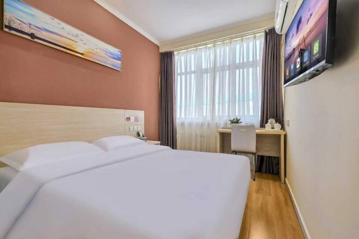 Ein Hotelzimmer mit einem großen Bett, einem Schreibtisch, einem Sessel, einem Fernseher und einem Fenster mit Vorhängen.
