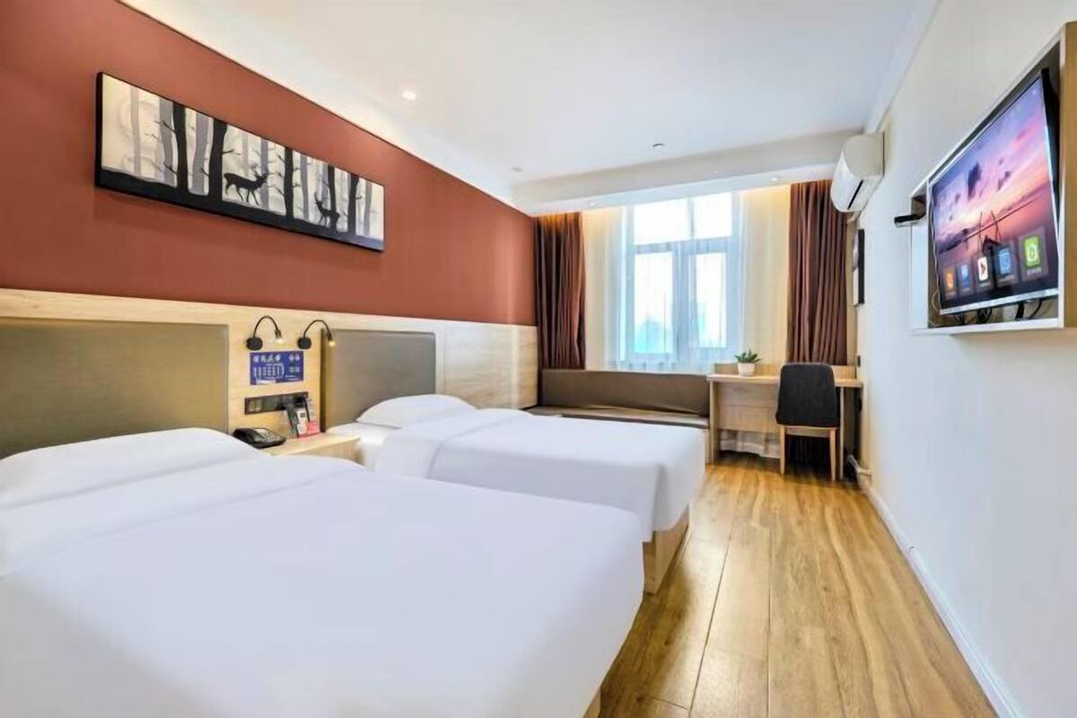 Ein Hotelzimmer mit zwei Betten, einem Schreibtisch, einem Stuhl, einem Fernseher und einem Fenster mit Vorhängen.