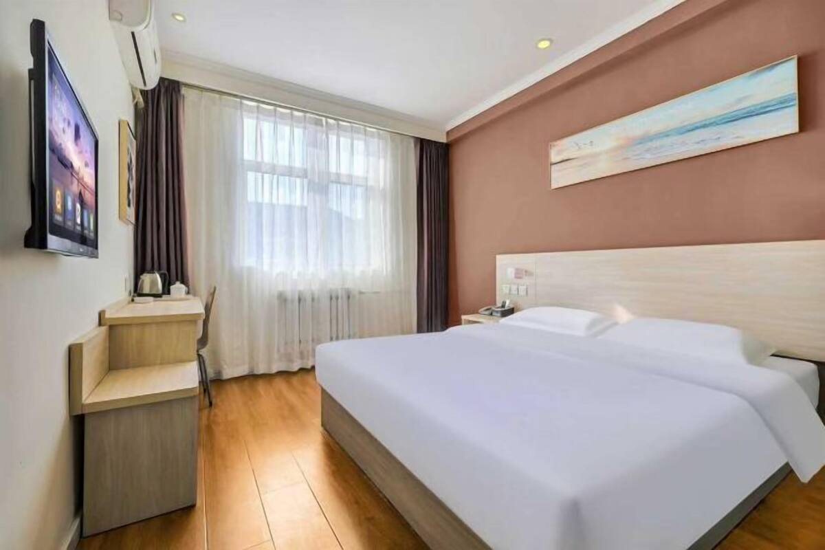 Ein Hotelzimmer mit einem Bett, einem Nachttisch, einem Fernseher, einem Fenster mit Vorhängen und einem Bild an der Wand.