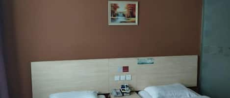 A hotel room with two single beds, a wooden headboard, a small bedside table with a phone, and a framed picture on the wall.