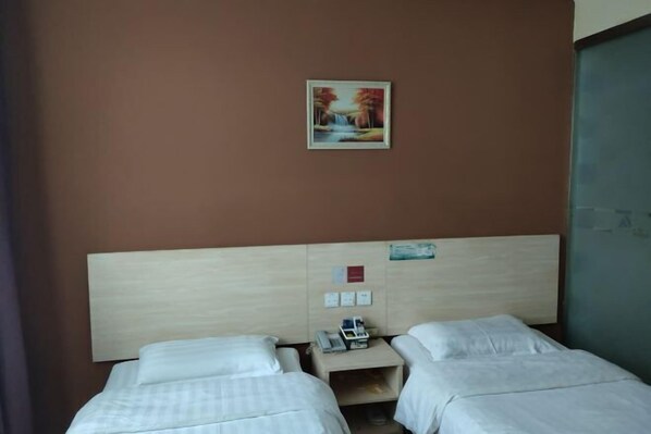 Ein Hotelzimmer mit zwei Einzelbetten, einem hölzernen Kopfteil, einem kleinen Nachttisch mit Telefon und einem gerahmten Bild an der Wand.