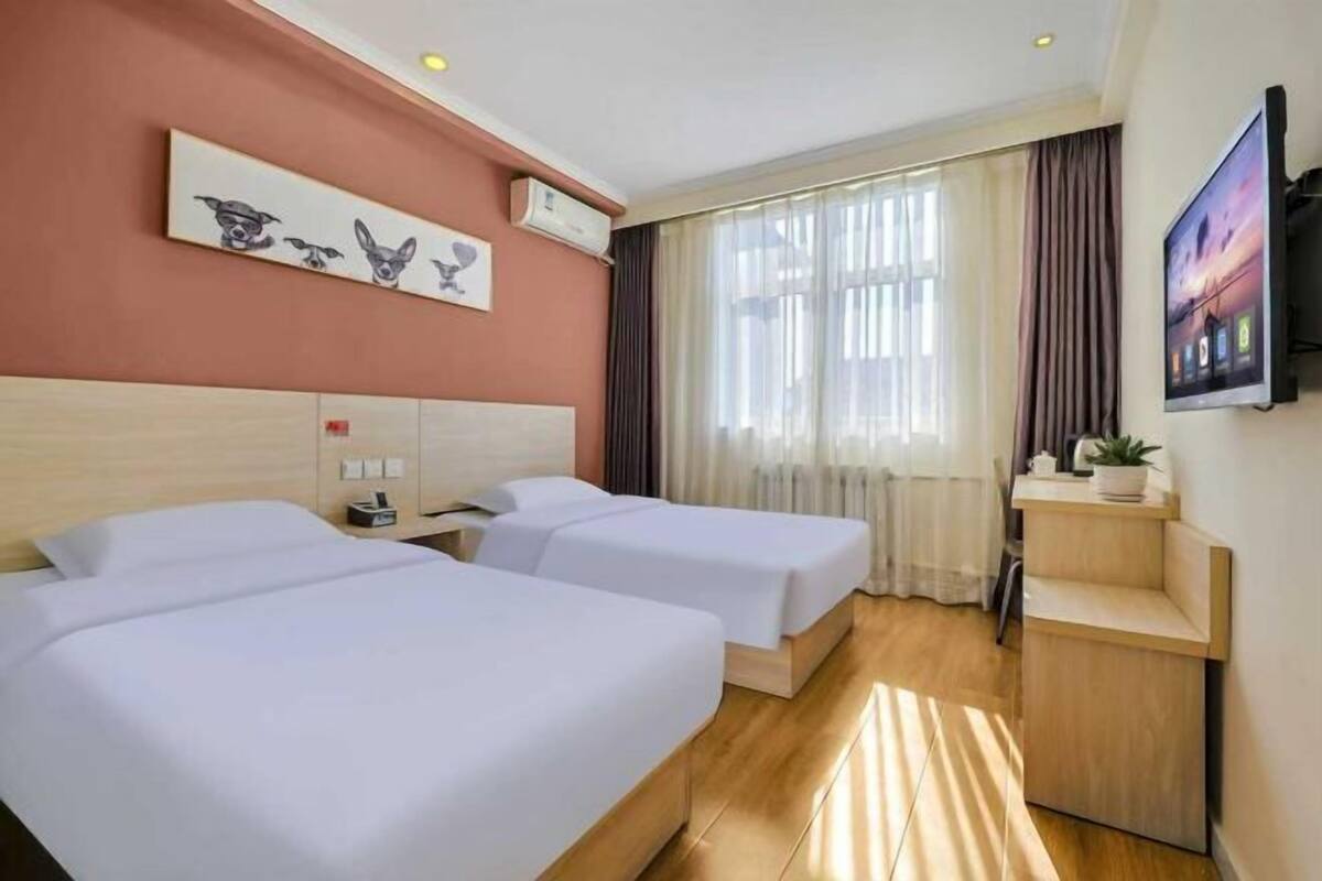 Ein Hotelzimmer mit zwei Betten, einem Fernseher, einem Schreibtisch und einem Fenster mit Vorhängen.