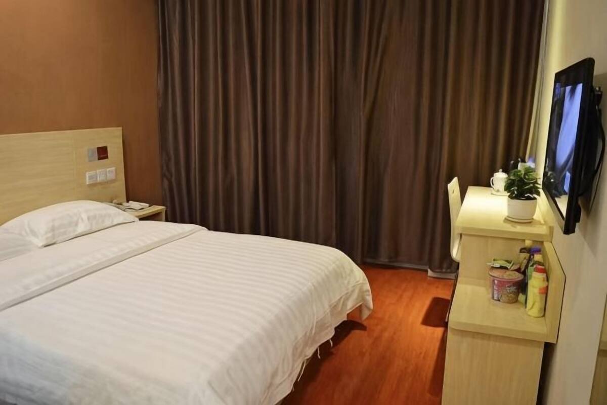 Ein Hotelzimmer mit einem Bett, einem Schreibtisch mit Pflanze und einem an der Wand befestigten Fernseher.