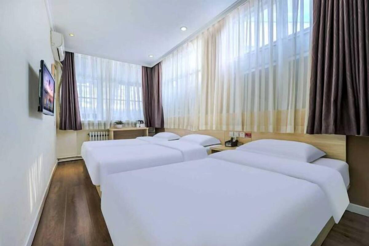 Ein Hotelzimmer mit zwei Betten, einem Fernseher, einem Schreibtisch und einem Fenster mit Vorhängen.