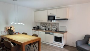 A modern kitchen with white cabinets, a microwave, a toaster, and a dishwasher. There is a dining table with chairs and a vase of flowers.