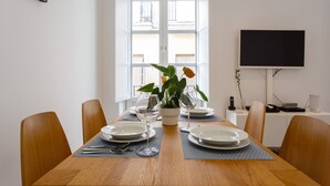 A dining table set with plates, glasses, and a potted plant, with a TV and desk in the background. - ALBA Apartment by Cadiz4Rentals (Cádiz)