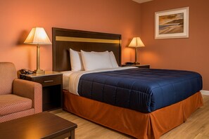 A hotel room with a large bed, two bedside lamps, a nightstand, a chair, and a wooden table.