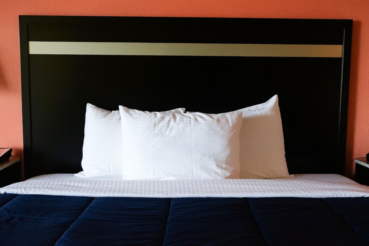 A bed with white pillows and a dark blue bedspread in a room with an orange wall.