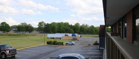 A parking lot with several cars and a truck, a building with a brick facade, and a grassy field in the background.