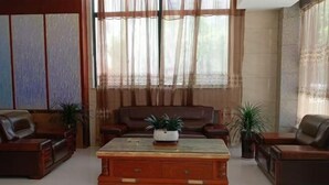 A spacious living room with a large window, leather sofas, a wooden coffee table, and potted plants. - Zhongchen Hotel (Chizhou Nanhu Road) (Chizhou)