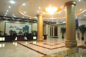 Una hall d'albergo con una reception, colonne imponenti, un lampadario e un quadro appeso al muro.
