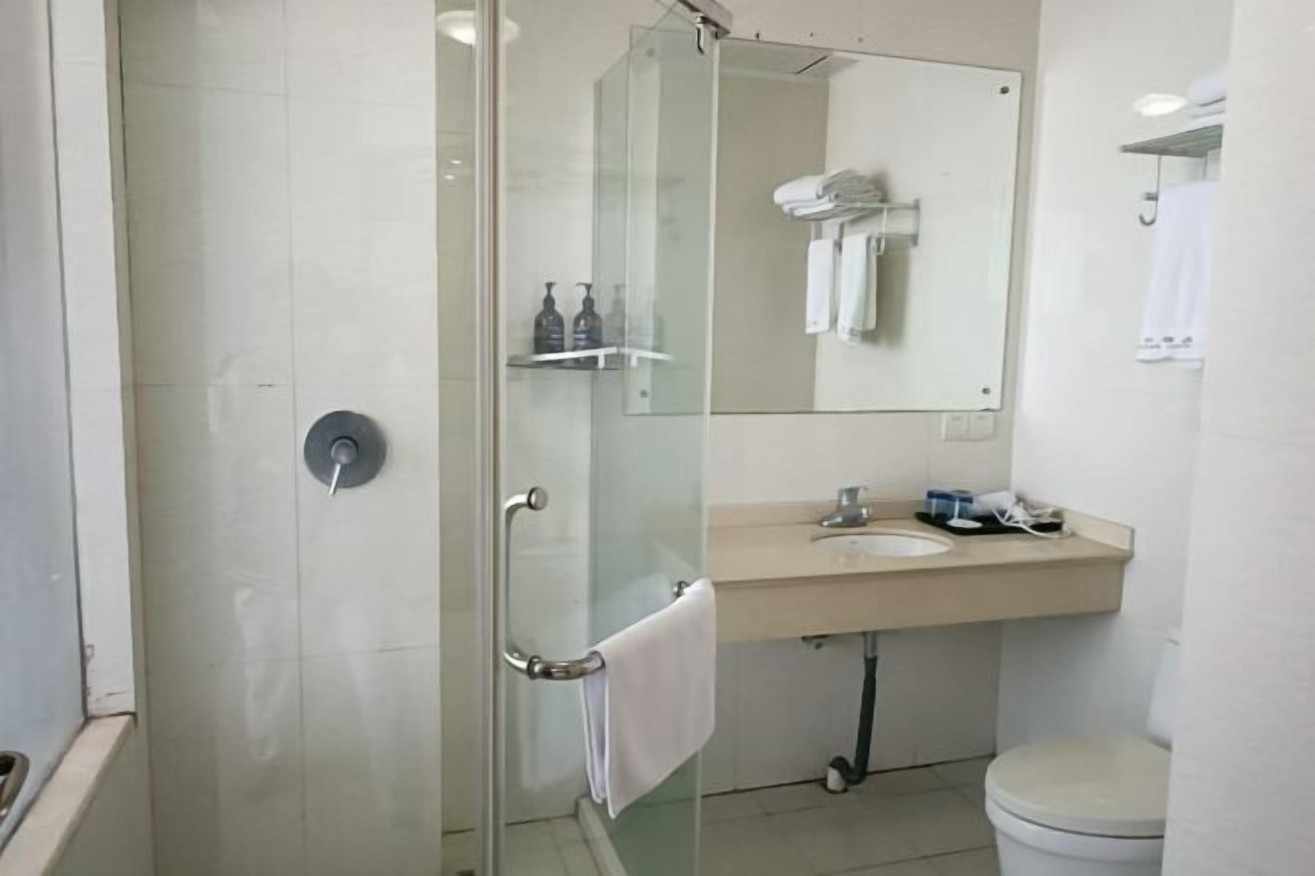 Et moderne badeværelse med glasvægs brusebad, vask med spejl og toilet.