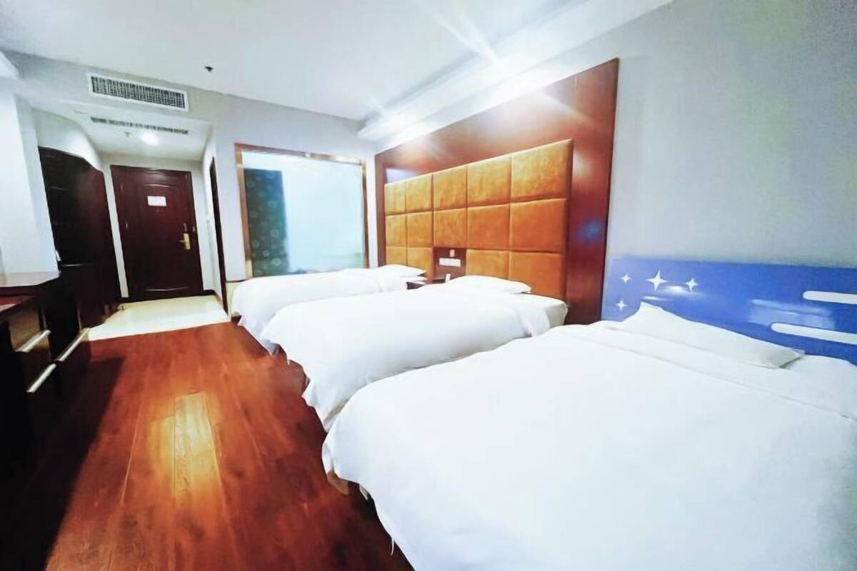 A hotel room with three single beds, wooden flooring, a large window, and a wall with a star pattern.