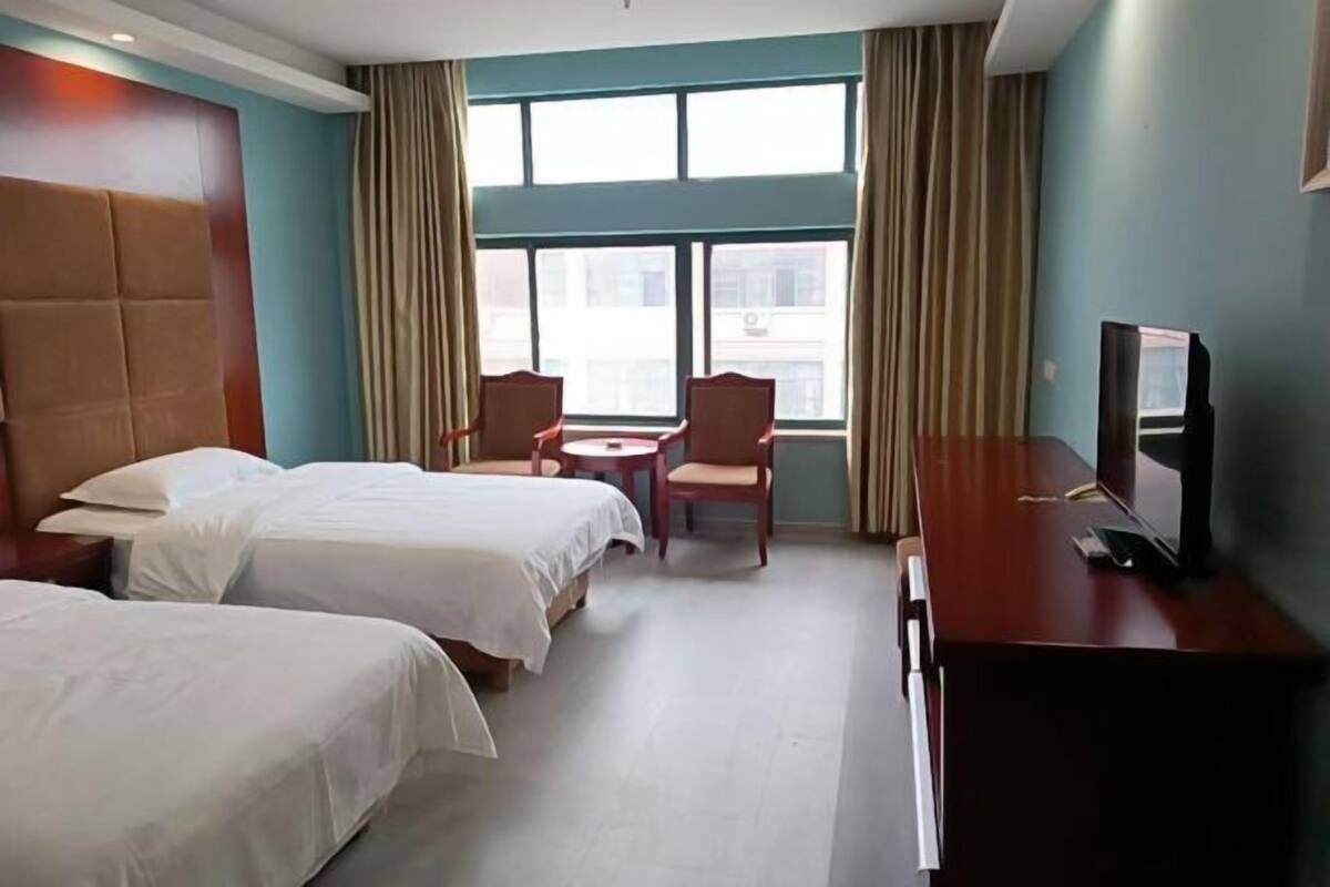 A hotel room with two beds, a desk, a chair, a TV, and a window with curtains.