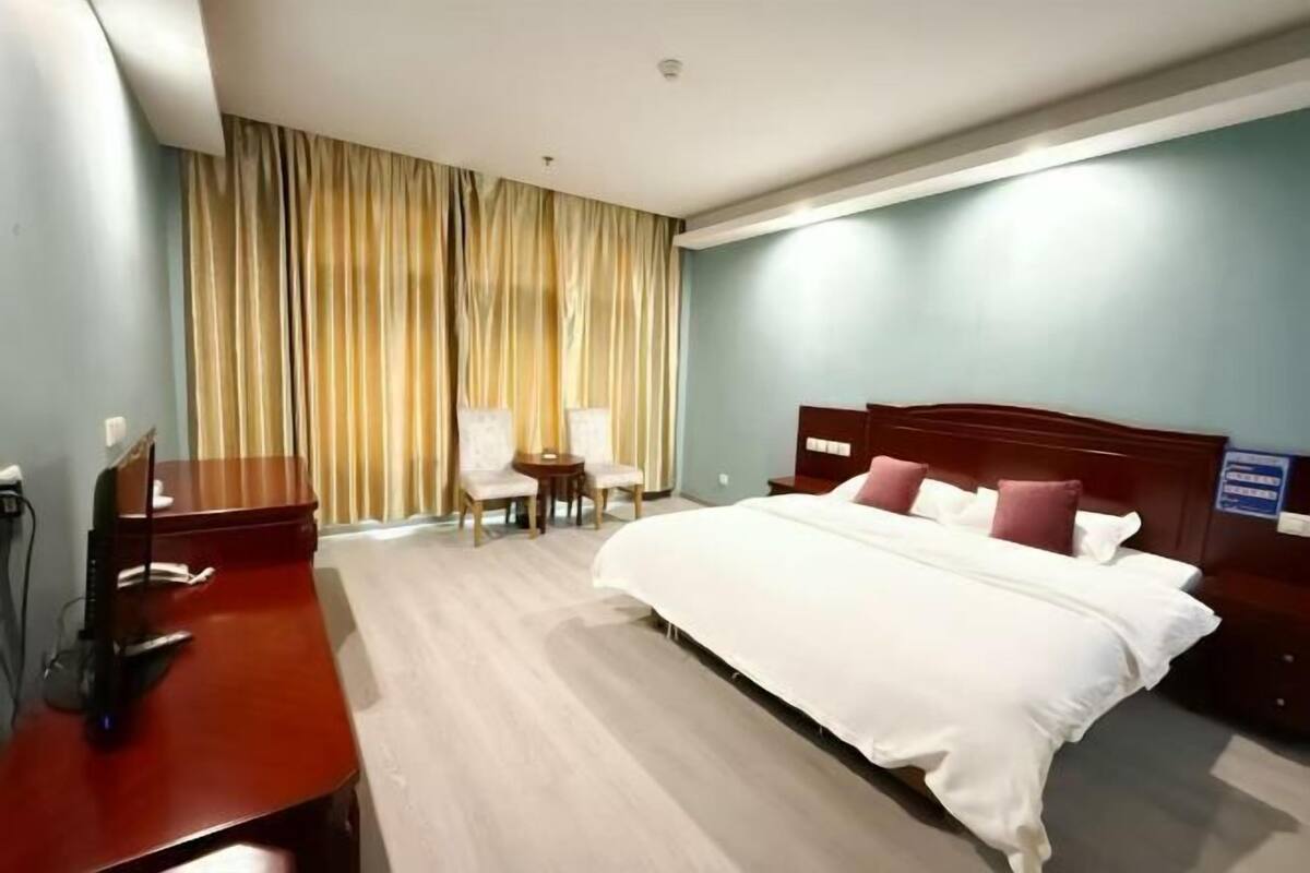 A hotel room with a bed, a desk, a chair, and a window with curtains.