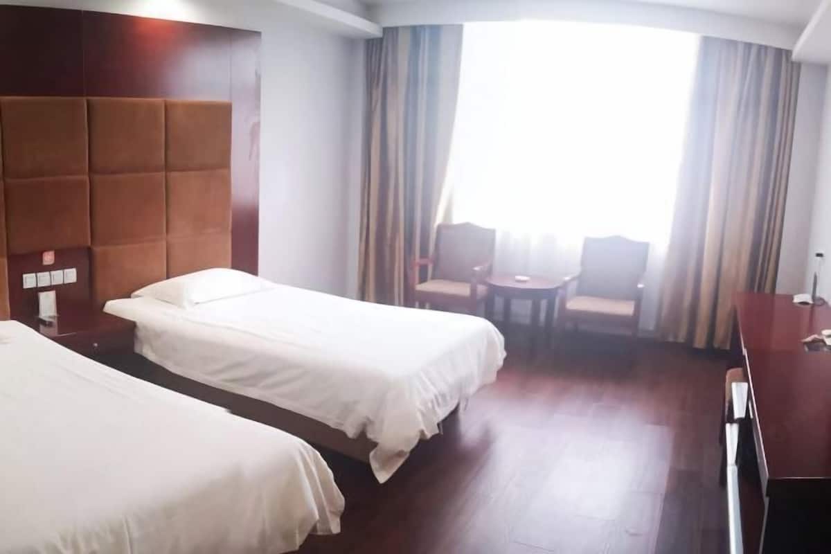 A hotel room with two beds, a wooden headboard, a small table, and a view of the outdoors.