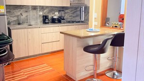 A modern kitchen with wooden cabinets, a granite countertop, a coffee maker, and a small island with bar stools.