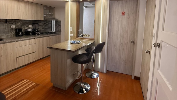 A modern kitchen with a marble countertop, wooden cabinets, and a built-in island with bar stools.