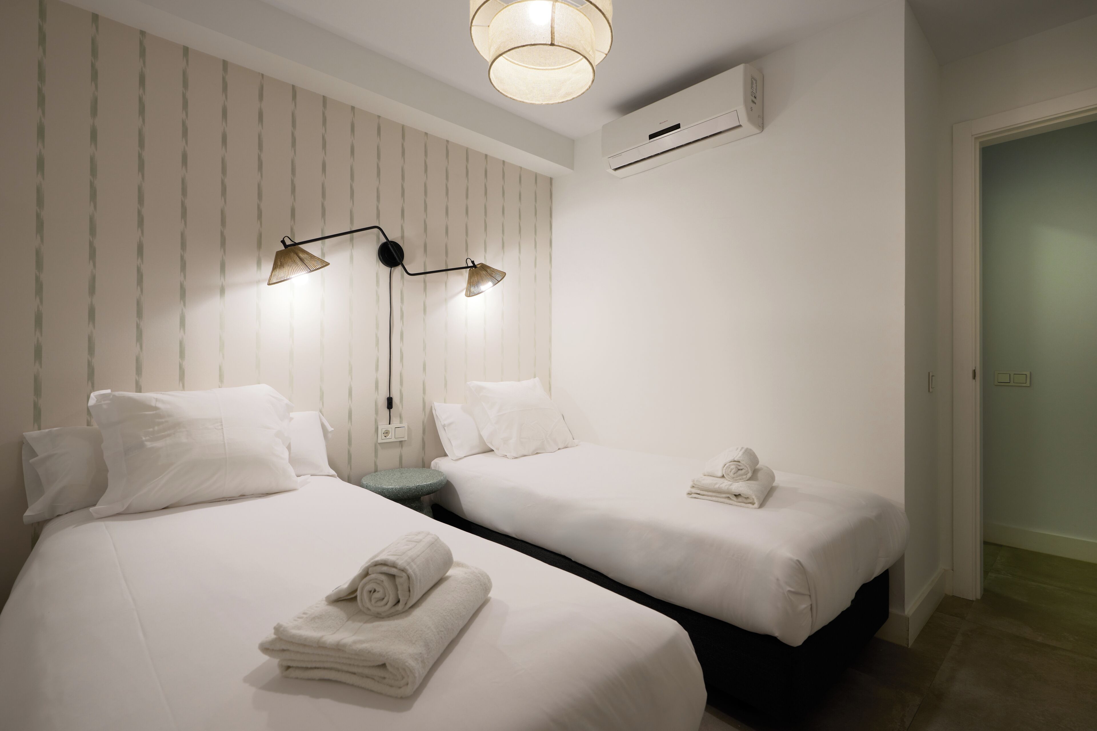 A hotel room with two beds, a nightstand, a lamp, and an air conditioning unit.