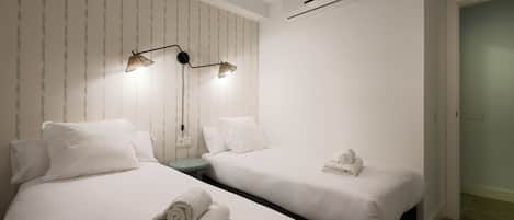 A hotel room with two beds, a nightstand, a lamp, and an air conditioning unit.