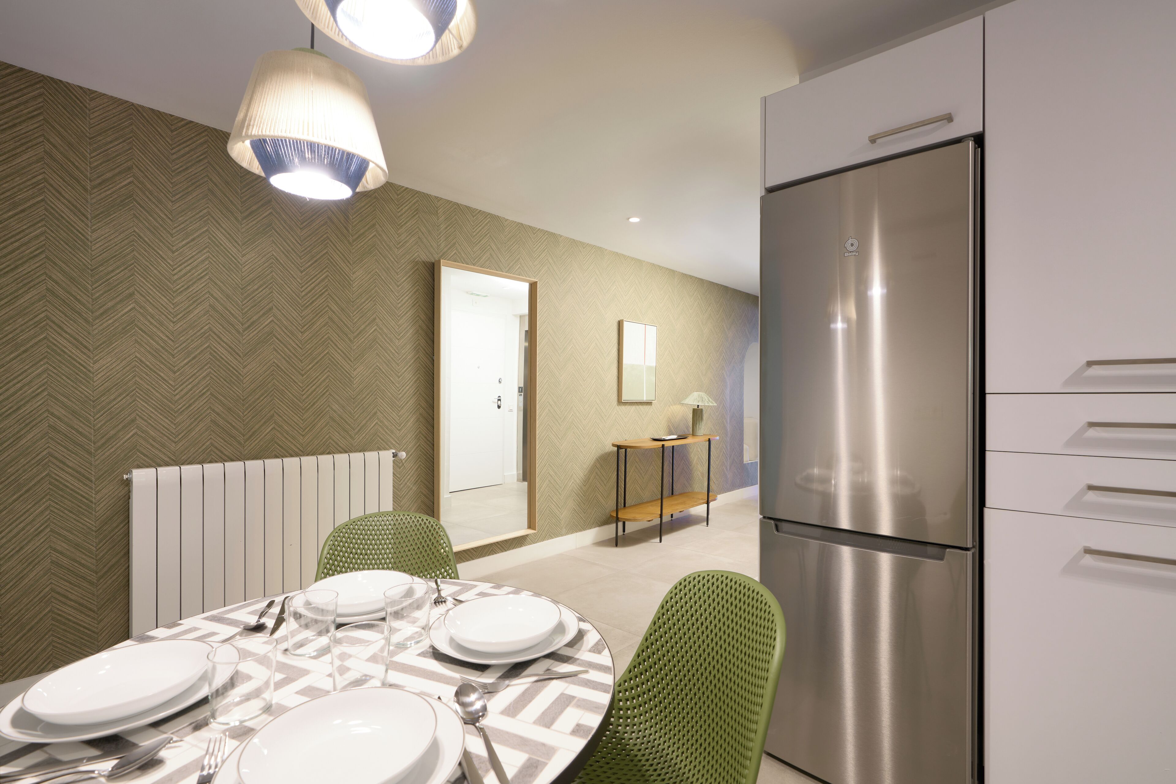 Una cocina moderna con un refrigerador de acero inoxidable, una mesa de comedor para cuatro personas y sillas verdes.