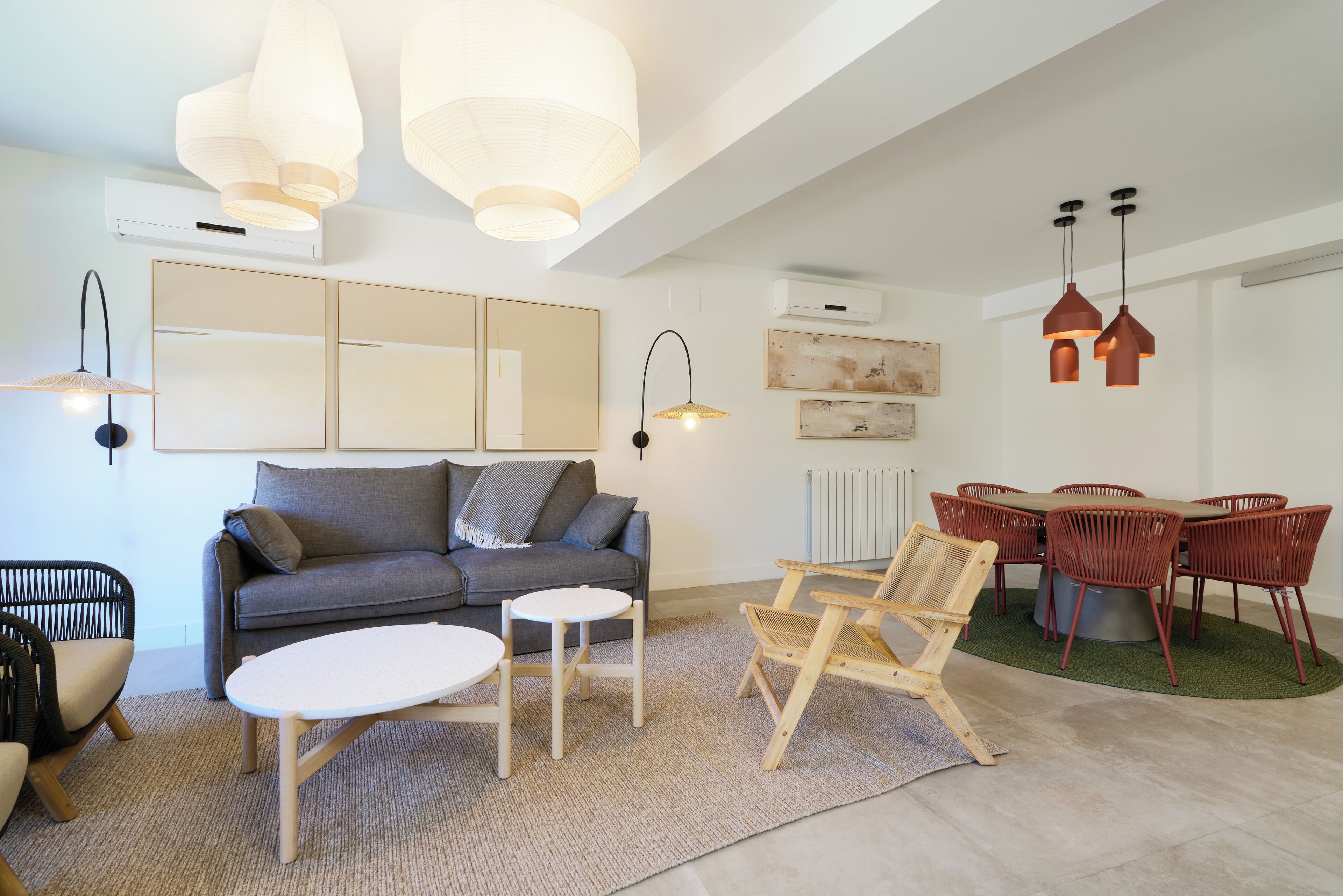 Un salon moderne avec un canapé gris, une table basse ronde et un coin repas comprenant des chaises rouges et une table.
