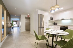 Una cucina moderna con mobili bianchi, un frigorifero in acciaio inossidabile e un'area pranzo con sedie verdi e un tavolo rotondo per quattro persone.