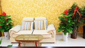 Un salón con un sofá, dos almohadones a rayas, una mesa de centro de vidrio y dos plantas en macetas con lazos rojos.