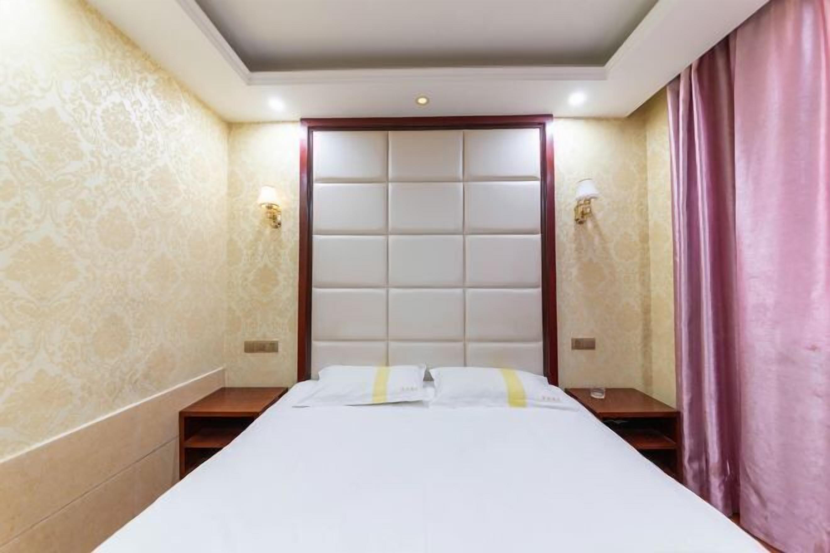 A hotel room with a large bed, a headboard with a padded design, two bedside tables, and a wall-mounted lamp.