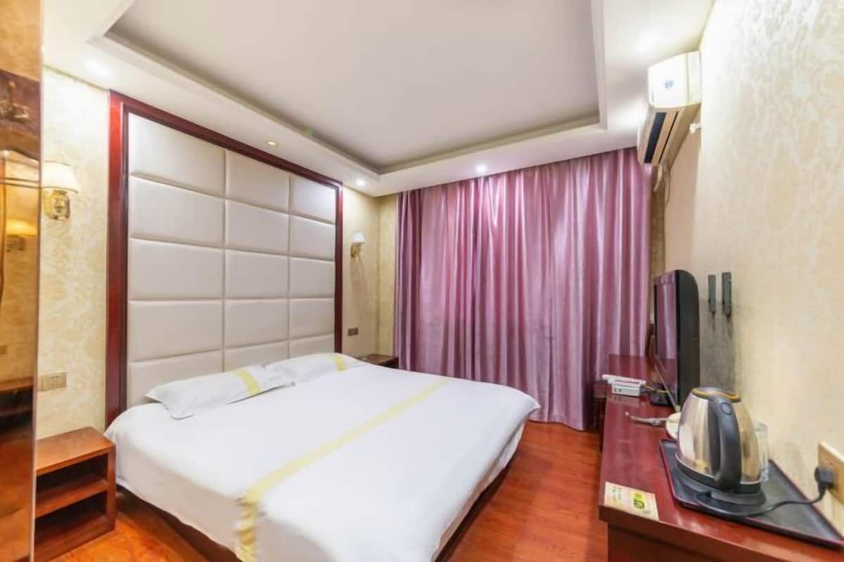 Ein Hotelzimmer mit einem großen Bett, einem Nachttisch aus Holz, einem Fernseher und einer Kaffeemaschine.