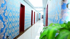 Un pasillo con paredes estampadas y puertas rojas, que conduce a un espacio luminoso.