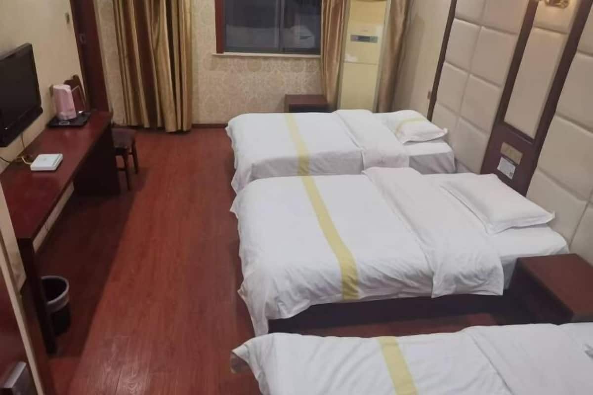 Ein Hotelzimmer mit zwei Betten, einem Fernseher, einem Schreibtisch und einem Fenster mit Vorhängen.