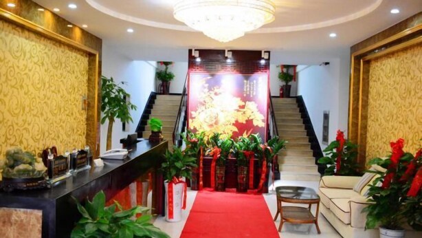 Un vestíbulo de hotel con una recepción, una alfombra roja, una escalera y un candelabro.