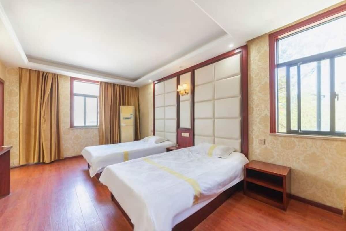 Ein Hotelzimmer mit zwei Betten, Holzboden, einem großen Fenster und einer Wandverkleidung im traditionellen Stil.