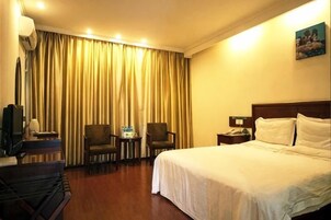 Quarto de hotel com cama, duas poltronas, uma mesinha, televisão e cortina.