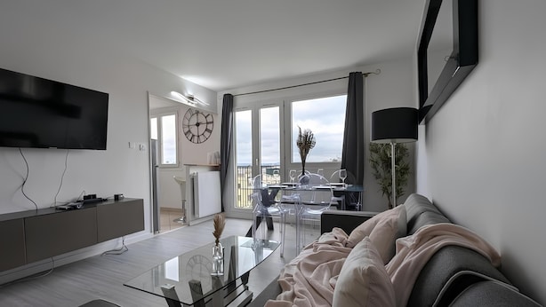 Una sala moderna con un televisor de pantalla plana, una mesa de centro de vidrio, un sofá y un comedor con una mesa y sillas de vidrio.